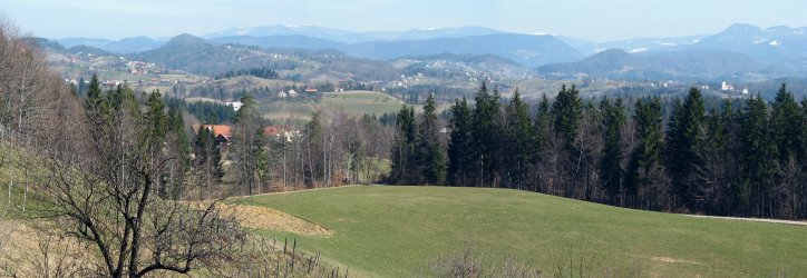Pogled preko travnikov na Velenjsko hribovje in Pohorje v ozadju