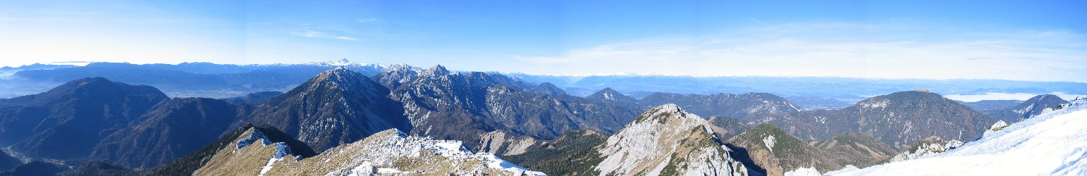 Pogled z Velikega vrha proti zahodu: Levo Dobrča, v sredini vrhovi Karavank, za njimi Julijske Alpe